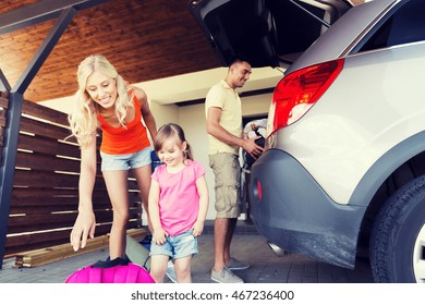 Transport, Leisure, Travel, Road Trip And People Concept - Happy Family Packing Things Into Car At Home Parking