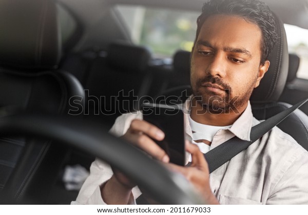 transport, people and technology\
concept - indian man or driver using smartphone in\
car