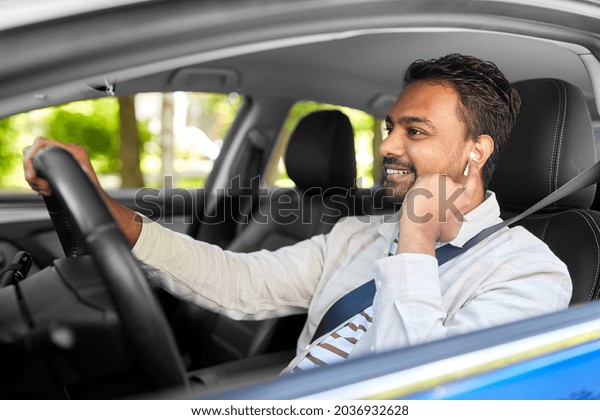 transport, people and technology concept - smiling\
indian man or driver with wireless earphones or hands free device\
driving car