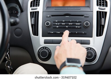 Transport, Road Trip, Car Driving, Technology And People Concept - Close Up Of Male Hand Turning On Radio On Control Panel System In Car