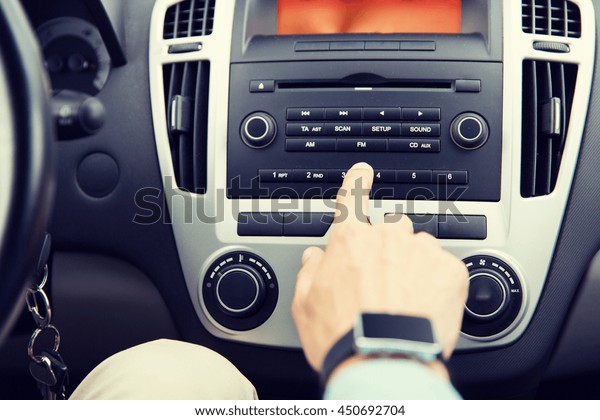 transport, road trip, car driving, technology and\
people concept - close up of male hand turning on radio on control\
panel system in car