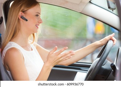 Transport and safety concept. Young blonde woman driving car using her mobile phone and headset, side view