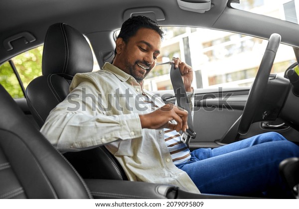 transport, safety and people\
concept - happy smiling indian man or driver fastening seat belt in\
car