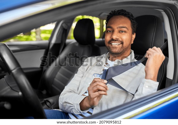 transport, safety and people\
concept - happy smiling indian man or driver fastening seat belt in\
car
