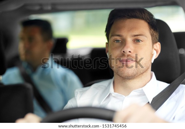 transport,\
taxi and people concept - male driver with wireless earphones or\
hands free device driving car with\
passenger