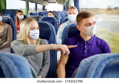 transport, tourism, road trip and people concept - young couple wearing face protective medical masks for protection from virus disease with group of tourists driving in travel bus