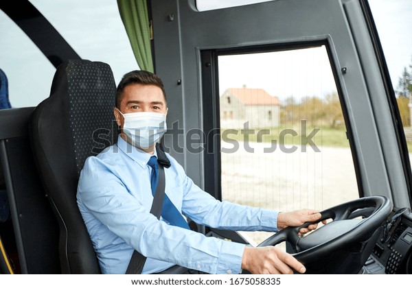 transport, travel and pandemic concept - male driver\
wearing protective medical mask for protection from virus disease\
driving intercity\
bus