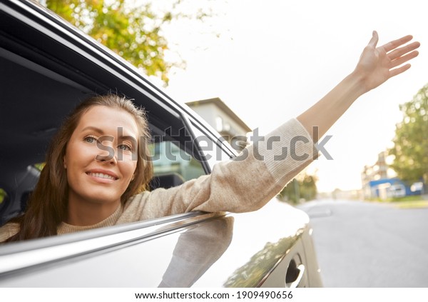 transport, vehicle and\
people concept - happy smiling woman or female passenger waving\
hand in taxi car