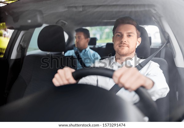 transport,\
vehicle and people concept - male driver with wireless earphones or\
hands free device driving car with\
passenger