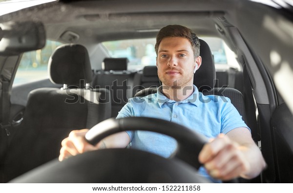 transport, vehicle and\
people concept - man or driver with wireless earphones or hands\
free device driving\
car