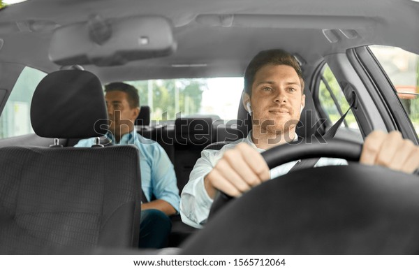 transport,\
vehicle and taxi concept - male driver with wireless earphones or\
hands free device driving car with\
passenger