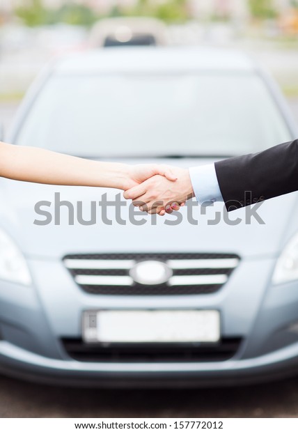 transportation, business, shopping\
and ownership concept - customer and salesman shaking hands\
outside