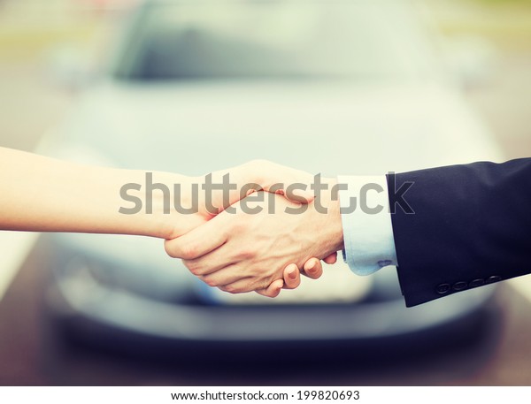 transportation, business, shopping\
and ownership concept - customer and salesman shaking hands\
outside