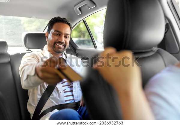 transportation and\
cash-free payment concept - happy smiling indian male passenger\
giving credit card to taxi car\
driver
