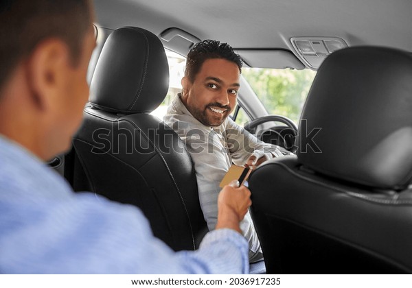 transportation and cash-free\
payment concept - indian male taxi car driver taking credit card\
from passenger