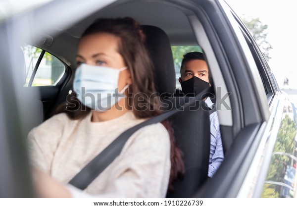 transportation, health and people concept -\
female driver driving car with male passenger wearing face\
protective medical mask for protection from virus\
disease