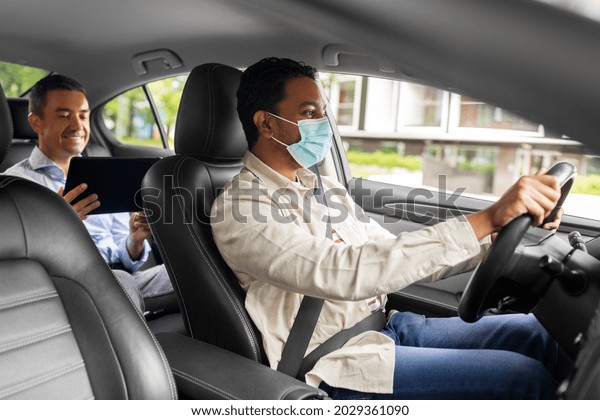 transportation, health and people
concept - indian male taxi driver driving car with passenger
wearing face protective medical mask for protection from virus
disease