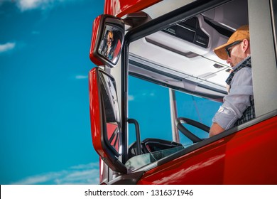 Transportation Industry Theme. Caucasian Truck Driver In His 30s Inside The Red Semi Cabin. 