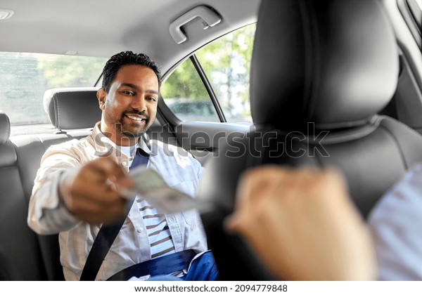 transportation and payment\
concept - happy smiling indian male passenger giving money to taxi\
car driver