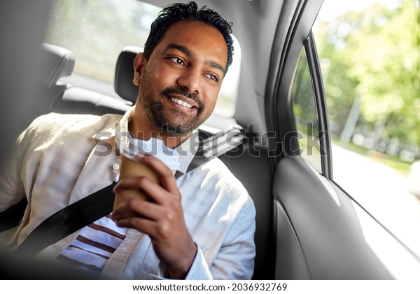 transportation and people\
concept - happy smiling indian man with takeaway coffee on back\
seat in taxi car