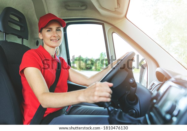 transportation services - young female\
driver in red uniform driving a van. smiling at\
camera