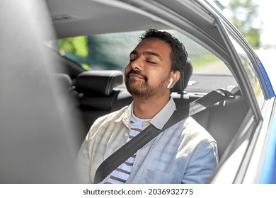 Transportation, Technology And People Concept - Happy Smiling Indian Male Passenger With Wireless Earphones On Back Seat Of Taxi Car