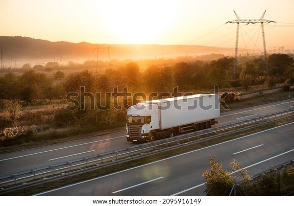 Transportation truck along the highway in\
dreamy sunset. Highway transportation with setting sun and hazy sun\
rays in the\
background