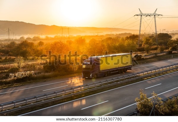 Transportation truck passing along highway in\
a dreamy sunset. Highway transportation with setting sun and hazy\
sun rays in the\
background