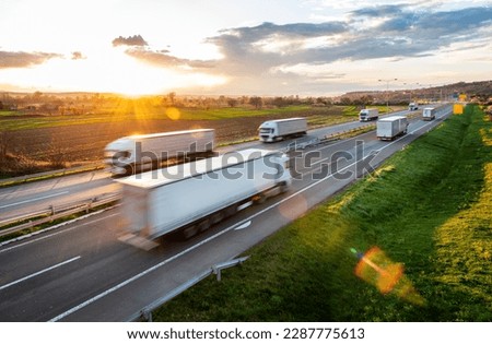 Transportation trucks in high speed driving on a highway through rural landscape. Fast blurred motion drive on the freeway. Freight scene on the motorway