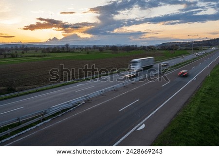 Transportation trucks in high speed driving on a highway through rural landscape. Fast blurred motion drive on the freeway. Freight scene on the motorway.