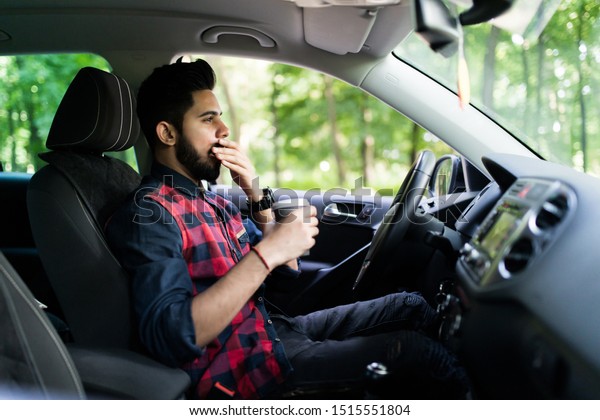 transportation and vehicle concept - man drinking\
coffee while driving the\
car