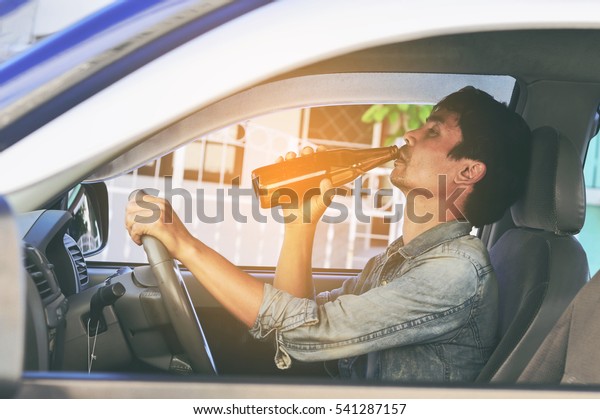transportation and vehicle concept - man\
drinking alcohol while driving the car . This is a campaign picture\
of \