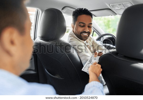transportation, vehicle and\
payment concept - passenger giving money to smiling indian male\
taxi car driver
