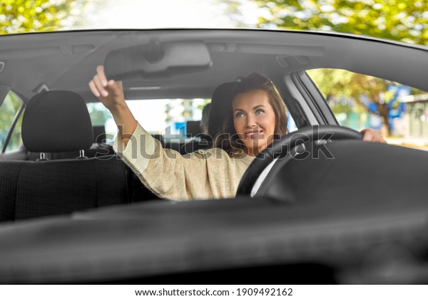transportation, vehicle and people concept -\
happy smiling female driver adjusting mirror and driving car with\
male passenger