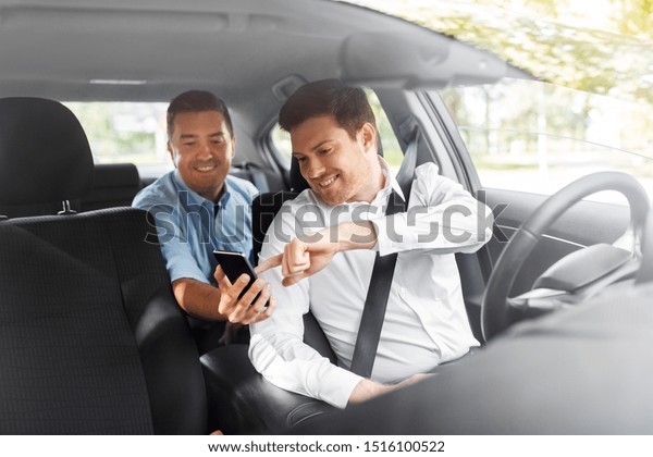 transportation,\
vehicle and technology concept - middle aged male passenger on back\
seat showing his smartphone to car\
driver