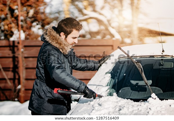 Transportation, vehicles, winter,\
people concept - man cleaning car from snow during cold sunny\
day