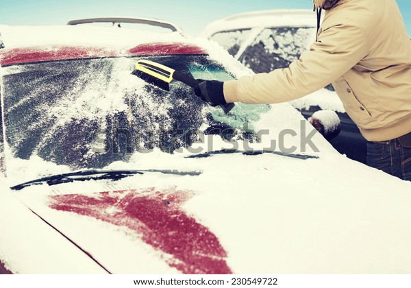 transportation, winter and vehicle\
concept - closeup of man cleaning snow from car windshield with\
brush