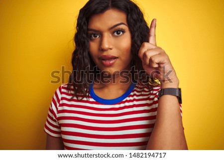 Transsexual transgender woman wearing stiped t-shirt over isolated yellow background surprised with an idea or question pointing finger with happy face, number one