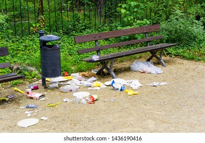 A Lot Of Trash Besides A Trash Can And A Brown Bank In A Park At Dresden, Germany. The Litter Is Most Likely Due To Some Birds Trying To Get Some Food.