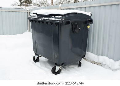 Trash container in winter surrounded by snow. Trees and grey sky on the background