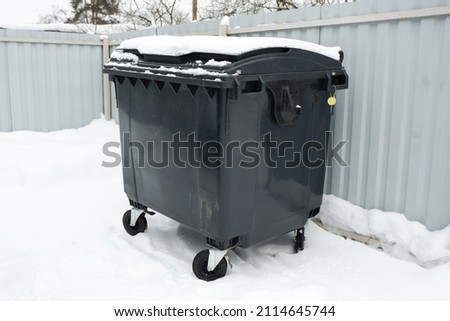 Trash container in winter surrounded by snow. Trees and grey sky on the background