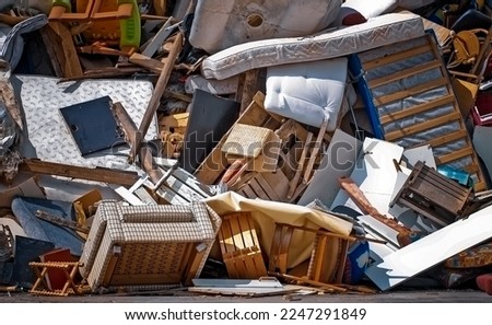Trash dump with old worn out mattresses, armchairs and other broken furniture of various shapes and colours.
