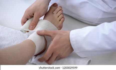 Traumatologist Applying Bandage To Sprained Ankle, Workout Injury, Leg Closeup