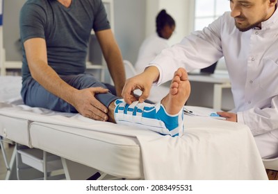 Traumatologist fixes orthopedic bandage on leg of male patient with fracture of ankle joint. Close up on examination couch injured leg of patient receiving first aid in trauma department. - Shutterstock ID 2083495531