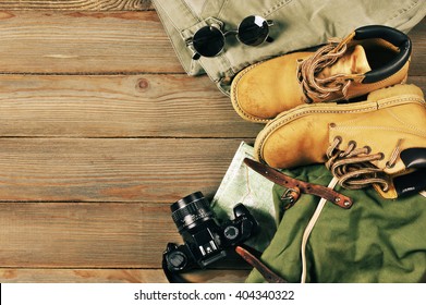 Travel accessories set on wooden background: old hiking leather boots, pants, backpack, map, vintage film camera and sunglasses. Top view point. - Shutterstock ID 404340322