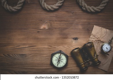 Travel or adventure flat lay background with a copy space. Binoculars, pocket watch, old parchment, mooring rope and a compass on a wooden table.