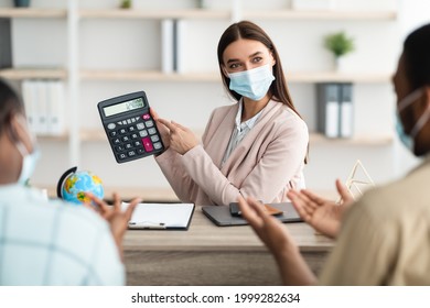 Travel Agency Service. Female Agent Showing Calculator With Price Of Family Tour Consulting African American Tourists Couple In Modern Office, Wearing Face Mask. Selective Focus, Cropped