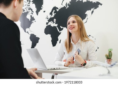 Travel Agent Having A Client In Light Modern Office Of Tour Agency, Giving Passport After Check-in Or Booking Flight. Assistant Keeps Tickets For The Plane In The Travel Agency To Clients. 