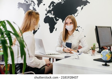 Travel Agent Having A Client In Light Modern Office Of Tour Agency, Choose Destination. Assistant Speaking In Face Mask In The Travel Agency To Clients. Protection During Covid Pandemic 