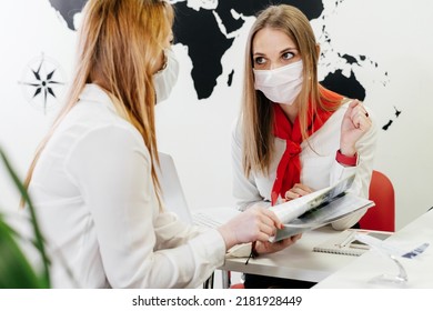 Travel Agent Having A Client In Light Modern Office Of Tour Agency, Choose Destination. Assistant Speaking In Face Mask In The Travel Agency To Clients. Protection During Covid Pandemic 